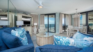 A spacious living room with a large sofa, a round coffee table, and a balcony with a dining area.