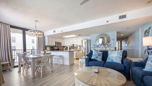 A modern living room with a blue sofa, a round coffee table, and a dining area with wooden chairs.