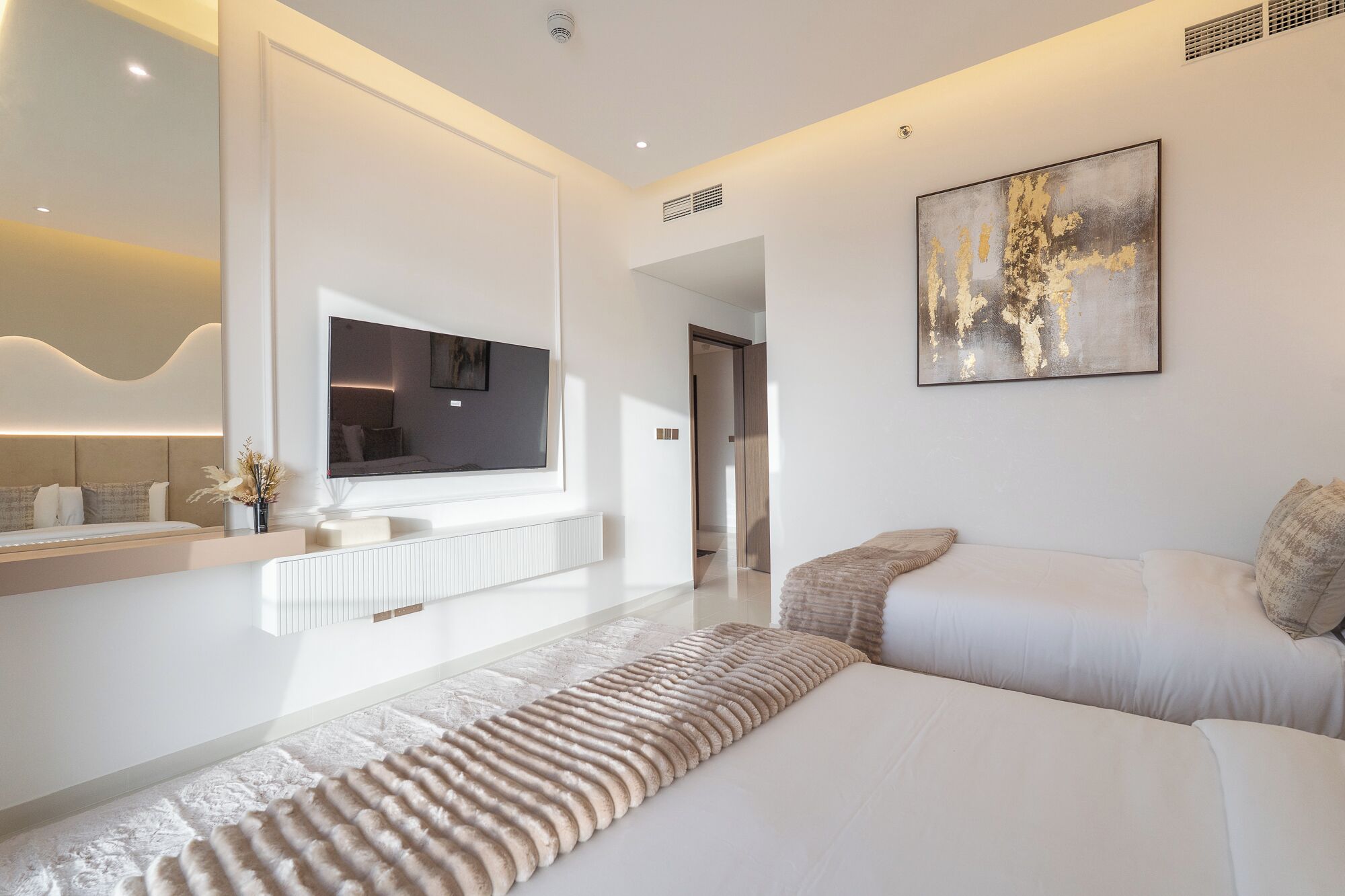 Quarto moderno com uma cama grande, televisão de tela plana, um quadro e área de banheiro com toucador e pia.