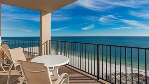 A balcony with a white table and chairs, overlooking a beach with clear blue water and a sandy shore. - Phoenix East 2 2153 3 Bedroom Condo (Orange Beach)