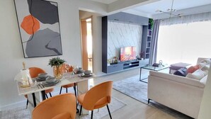 A modern living room with a fireplace, a dining area with orange chairs, and a large abstract painting on the wall. - leo residence (Nairobi)