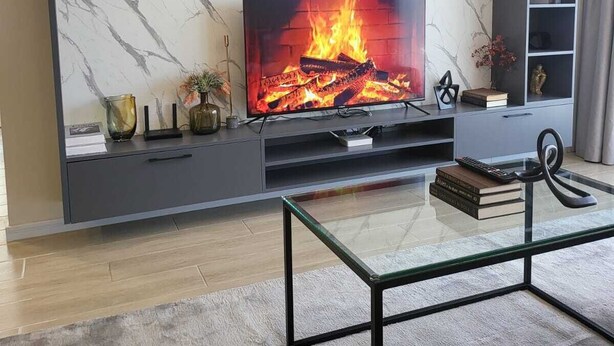 A modern living room with a marble-patterned wall, a flat-screen TV, a glass coffee table, and a bookshelf with decorative items. - leo residence (Nairobi)