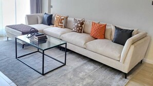 A modern living room with a beige sofa, a glass coffee table, and a grey rug. - leo residence (Nairobi)