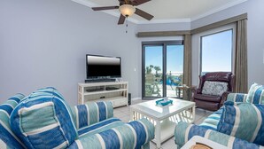Ein Wohnzimmer mit gestreiften Sofas, einem Flachbildfernseher, einem Deckenventilator und einem Balkon mit Gartenmöbeln.