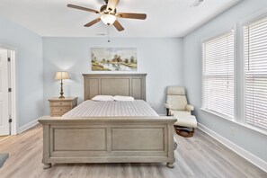 A bedroom with a bed, nightstand, lamp, chair, and a ceiling fan.
