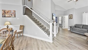 Una sala de estar moderna con una escalera, una zona de comedor y un sofá gris.