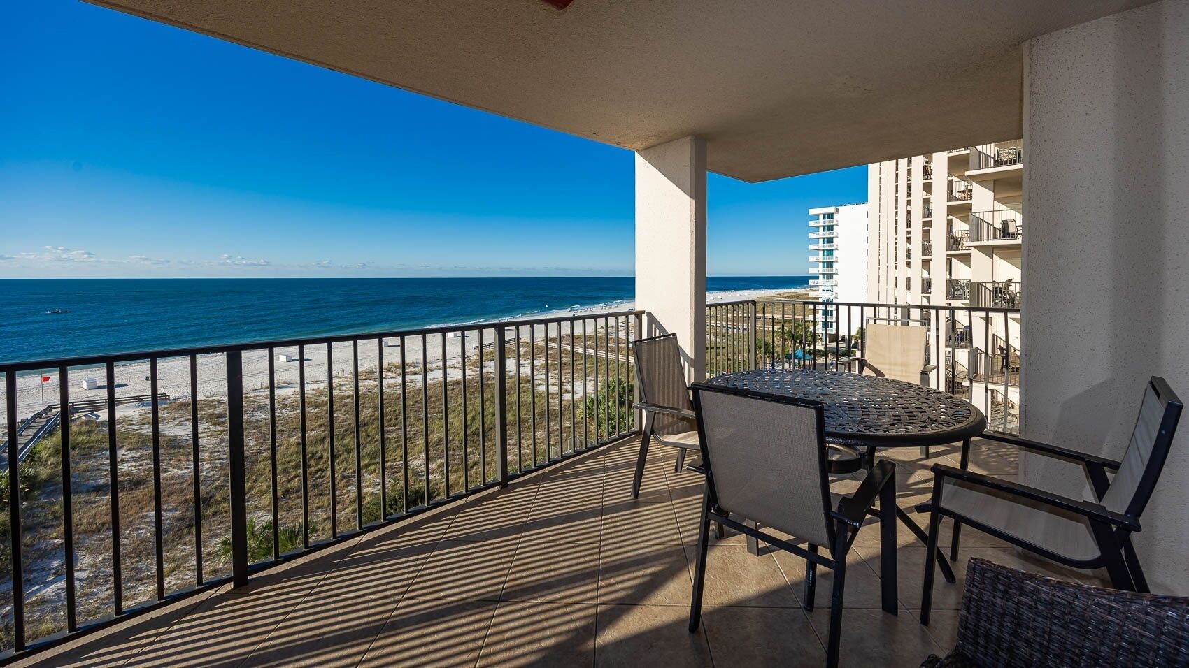 A balcony with a table and chairs, overlooking a beach and ocean.