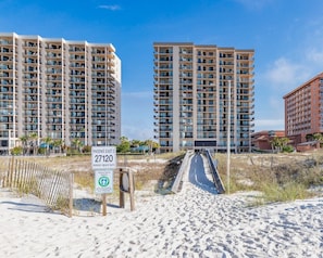 A beachfront hotel with multiple high-rise buildings, a sandy beach, and a sign indicating the address. - Phoenix East 2 2061 3 Bedroom Condo (Orange Beach)