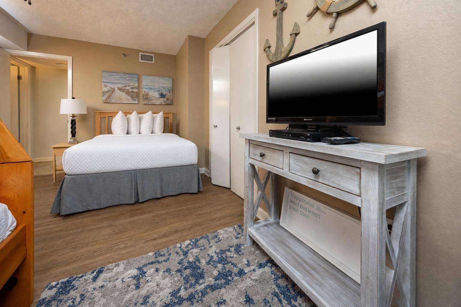 A hotel room with a bed, a television on a wooden console, a rug, and artwork on the wall.