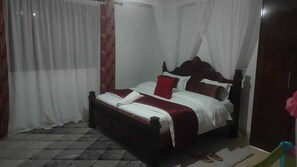 A bedroom with a bed, curtains, and a wooden headboard. - Lux Suites N&R Staycation Migori (Migori)