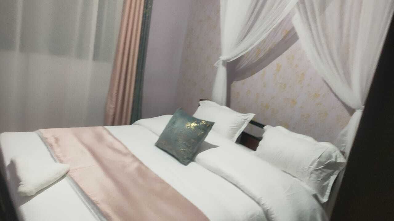Una cama con ropa de cama blanca, una única almohada decorativa, una manta rosa y un dosel.