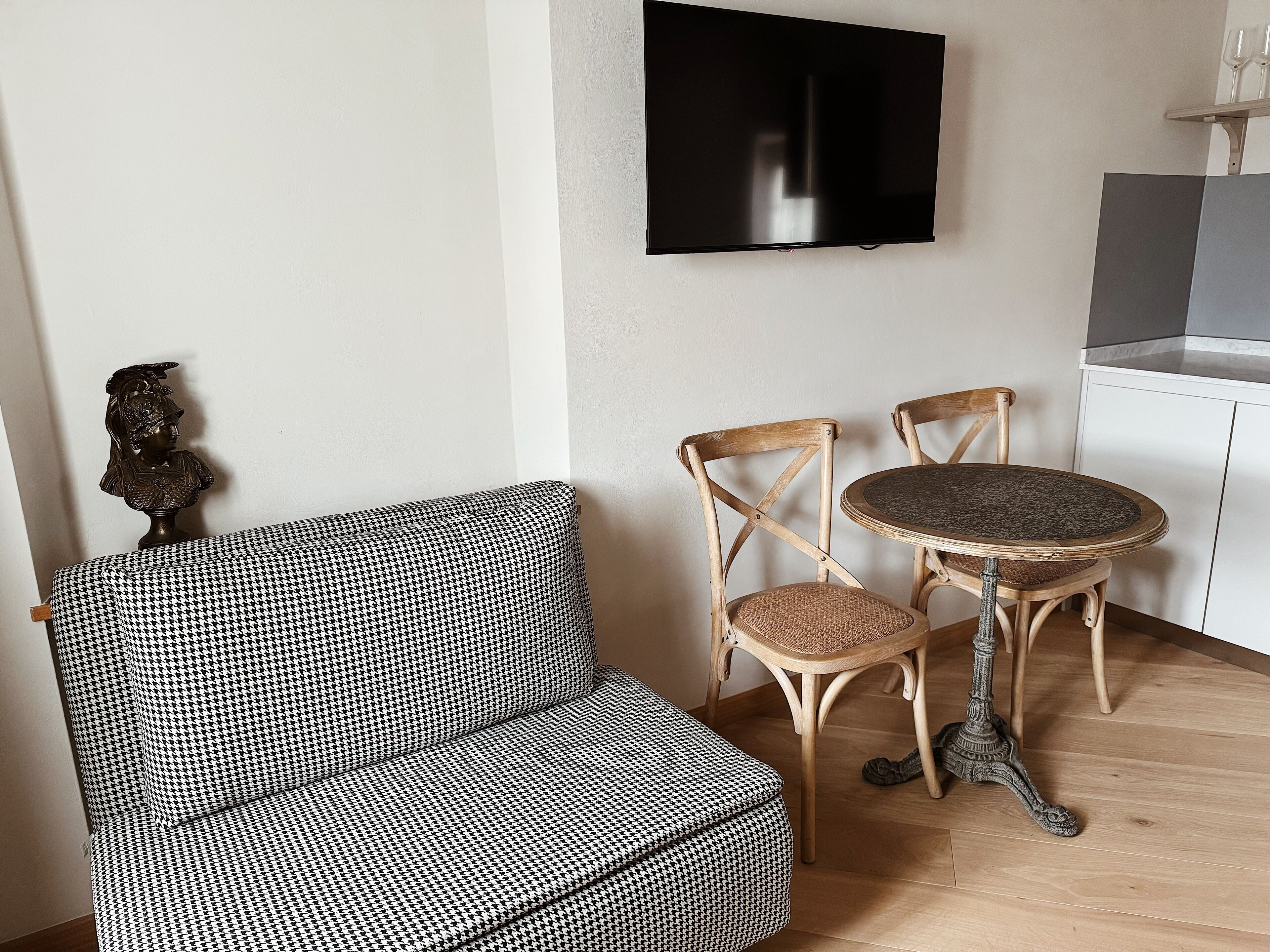 Una habitación con un sofá a cuadros Príncipe de Gales, dos sillas de madera, una mesa redonda y un televisor montado en la pared.