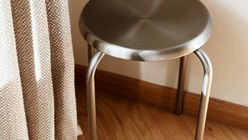 A small, round, metal-framed stool with a smooth surface, positioned on a wooden floor next to a beige curtain.