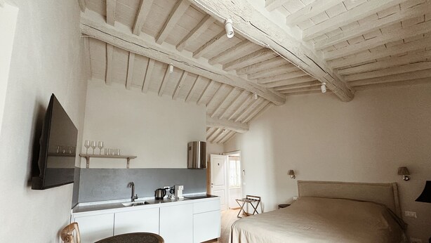 A bedroom with a bed, a small table, and a kitchenette with a sink and a stove. - Villa Sofia (Querceta)