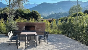 An outdoor seating area with a wooden table and chairs, surrounded by gravel, with a view of mountains and greenery in the background. - Villa Sofia (Querceta)