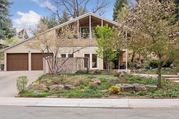 A two-story house with a garage, a covered porch, and a landscaped front yard with rocks and plants.