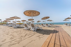 Ein Strand mit Reihen von Liegestühlen und Reetdachschirmen.