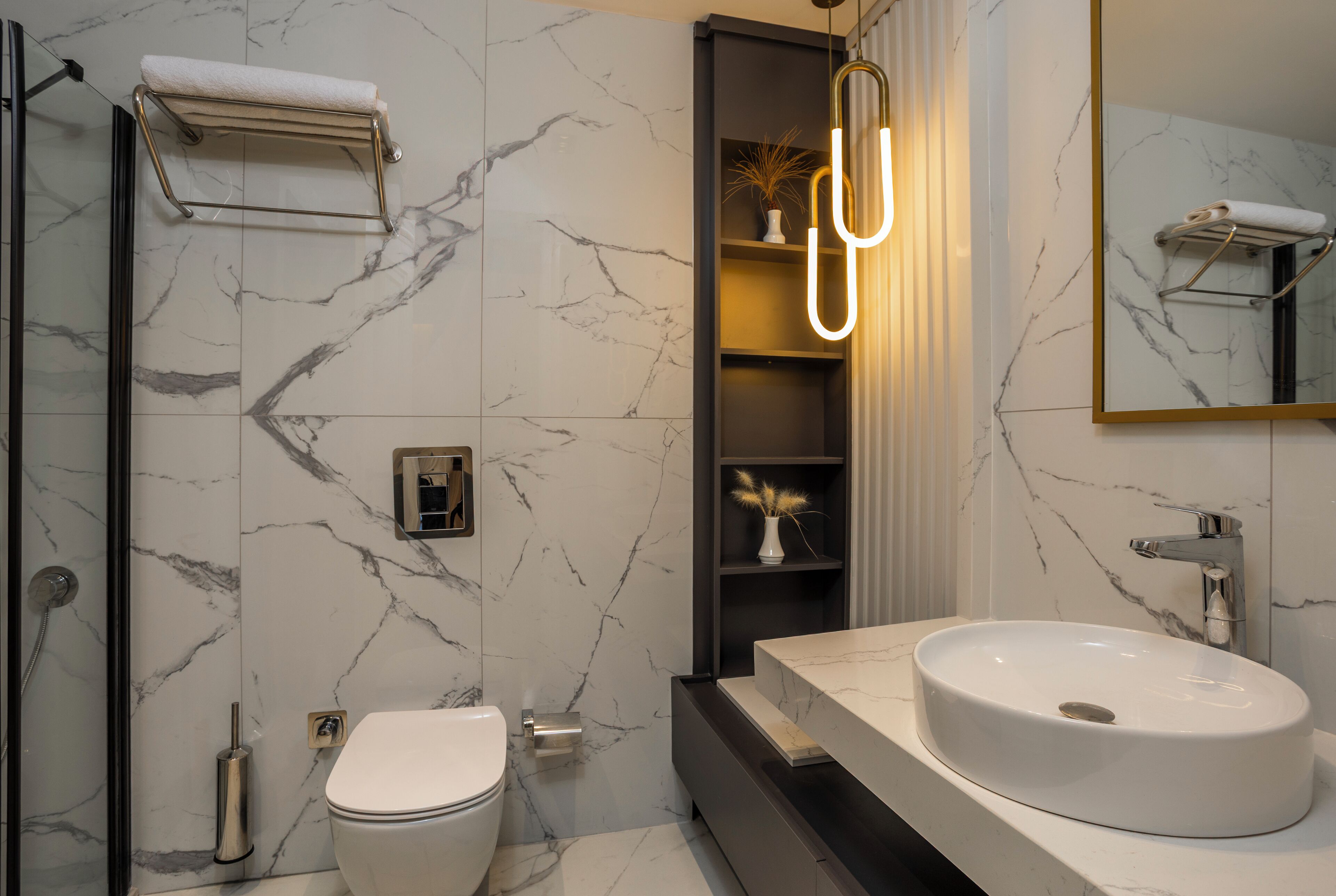 Ein modernes Badezimmer mit Marmor-Spritzschutz, einem weißen Waschbecken, einer Duschkabine aus Glas und einem Handtuchhalter.