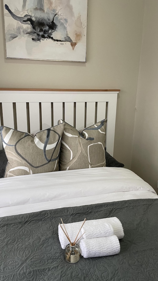 A neatly made bed with a grey patterned bedspread, two pillows with a geometric design, and a white headboard.
