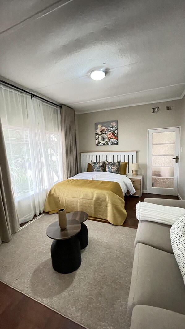 A hotel room with a bed, a sofa, a small table, and a window with curtains. - The Comfy Private Place - 2296 (Harare)