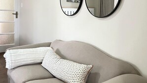 A neutral-colored sofa with a white and black polka dot pillow, two wall-mounted mirrors, and a floral painting. - The Comfy Private Place - 2296 (Harare)