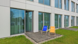 Un edificio moderno con ventanas amplias y una terraza de madera con dos sillas de playa.