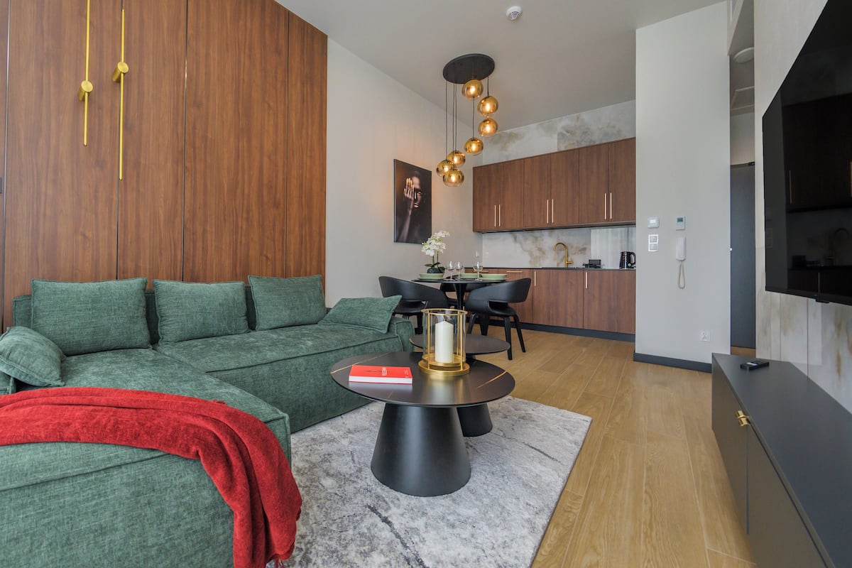 A modern living room with a green sofa, a red throw blanket, and a dining area with a black table and chairs.