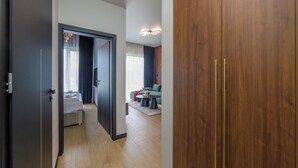 Habitación de hotel moderna con un armario de madera, una cama con edredón blanco, una pequeña mesa con una vela y un sofá verde en la sala de estar.