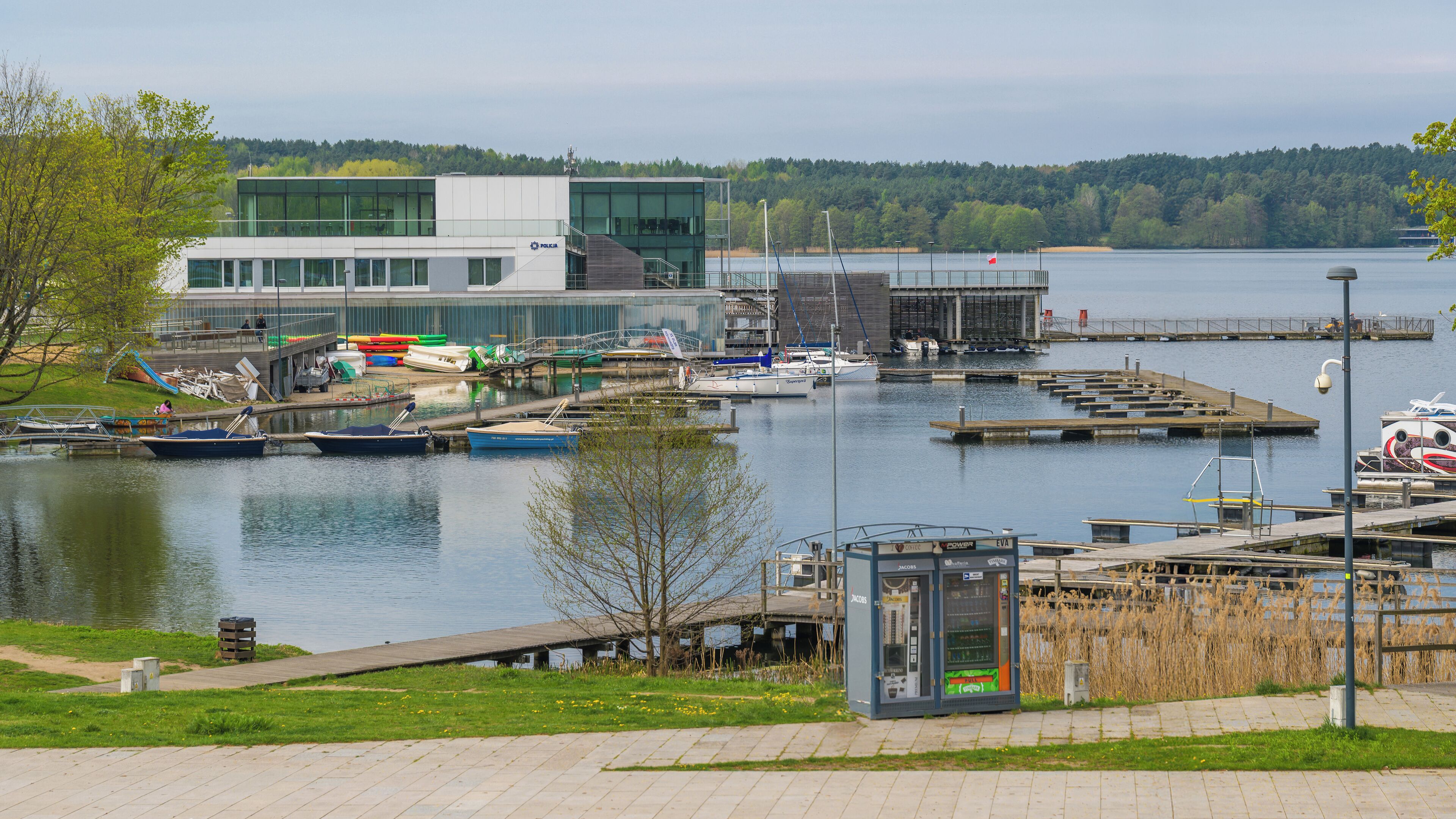 Een jachthaven met aangemeerde boten, een modern gebouw en een gazon met een automaat.
