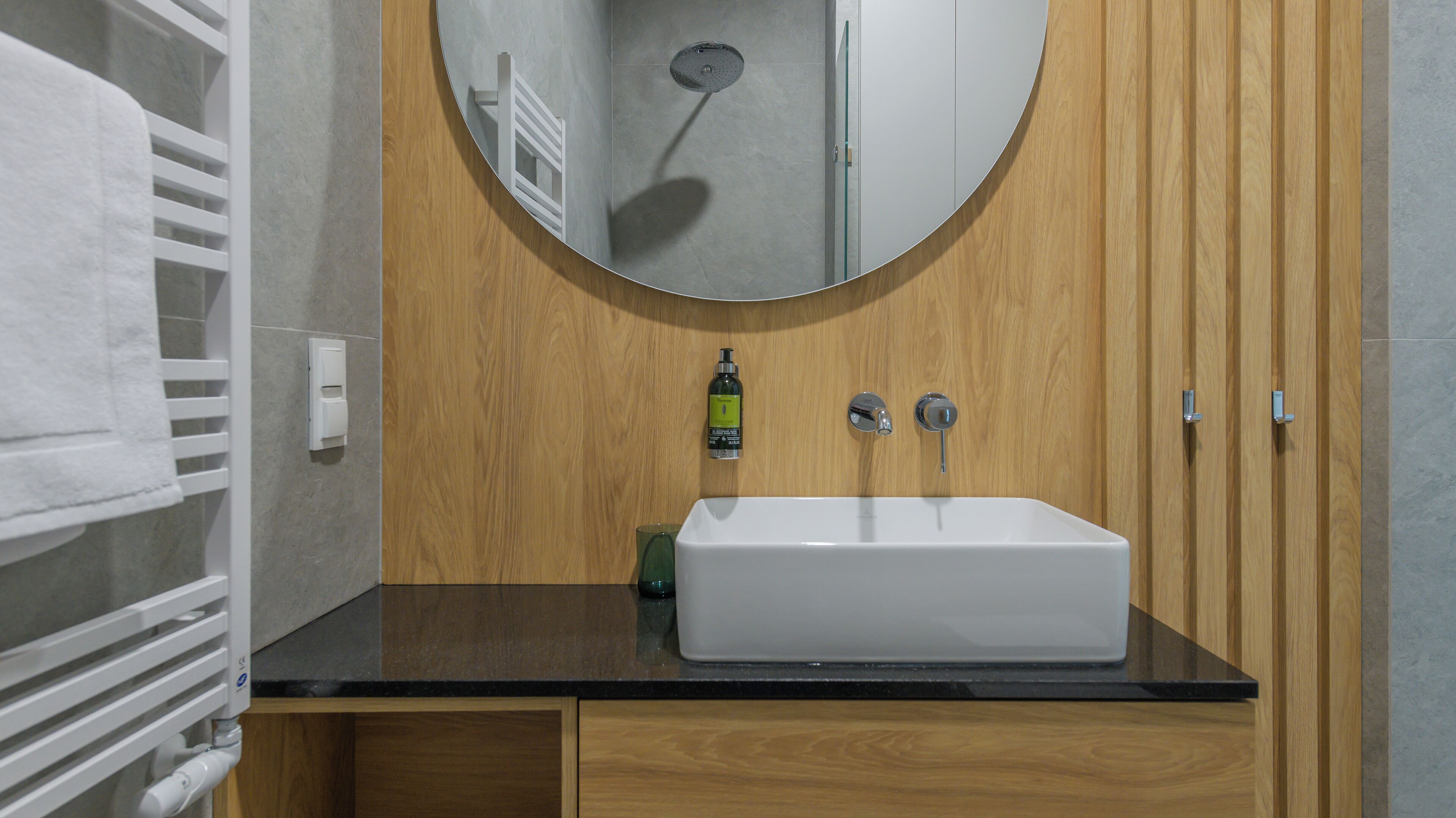 A bathroom with a white sink, wooden vanity, and a round mirror.
