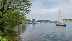 Un lago tranquilo con barcos, un muelle y un edificio moderno con ventanales de vidrio.