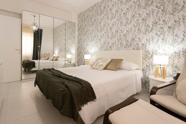 A modern bedroom with a large bed, a mirror, a nightstand, and a chair.