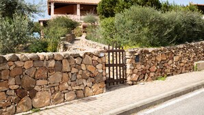 A stone wall with a gate, a paved path, and a building with a tiled roof in the background. - Casa Abba by Wonderful Italy (Golfo Aranci)