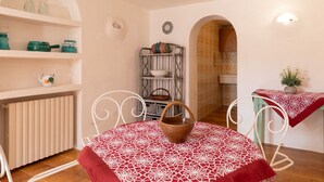 A dining area with a table set for two, a radiator, shelves with kitchen items, and a decorative wall piece. - Casa Abba by Wonderful Italy (Golfo Aranci)