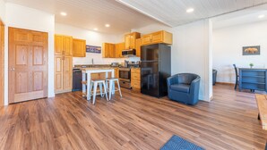 A modern kitchen with wooden cabinets, a black refrigerator, and a dining area with stools.