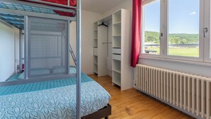 Una cama individual superpuesta con un edredón estampado, un armario con estantes y vistas a un paisaje verde por la ventana.
