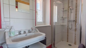 Un baño con lavamanos blanco, un espejo, cabina de ducha de vidrio y una ventana.