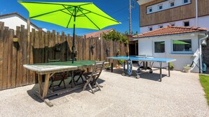 Un patio con una mesa y sillas de madera, una sombrilla verde y una mesa de ping pong.