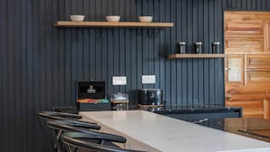A modern kitchen with a central island, black chairs, wooden cabinets, and built-in shelves with bowls and cups.