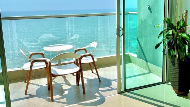 Un balcon avec une porte vitrée, une petite table, deux chaises et une plante en pot.
