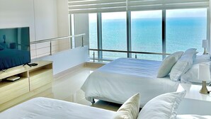 Une chambre d’hôtel moderne avec une vue imprenable sur l’océan, deux lits, une télévision et un design minimaliste.