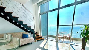 Un salon moderne avec un escalier, un canapé, une table en verre et une vue sur l’océan.