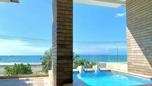 Un espace piscine moderne avec des parois en verre transparent, une vue sur l’océan et une terrasse en bois.