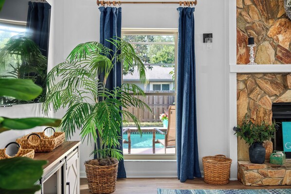 A room with a large window, a stone fireplace, and a view of a swimming pool.