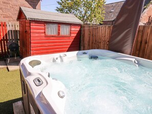 A hot tub in a backyard with a red wooden shed and a wooden fence. - Smiddy Bothy (Brechin)