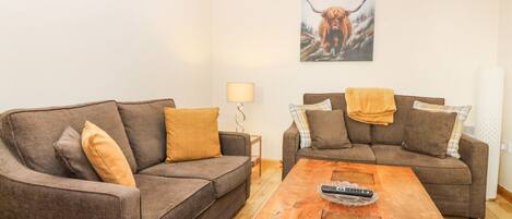 Een woonkamer met twee bruine banken, een houten salontafel en een schilderij van een stier aan de muur.