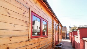 Una cabaña de madera con puerta y ventanas rojas, un sendero estrecho y una pared también roja.