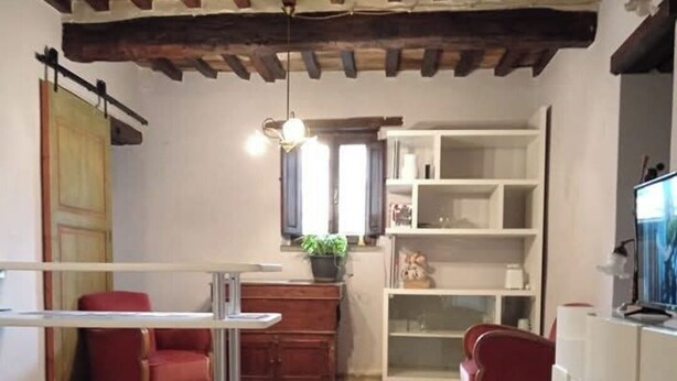 A cozy living room with a stone floor, a red sofa, a wooden cabinet, and a TV on a white stand. - Cozy detached house in the historic center of Umbertide indoor garden (Umbertide)