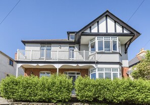 Two-story building with a balcony and gabled roof, surrounded by well-maintained hedges.