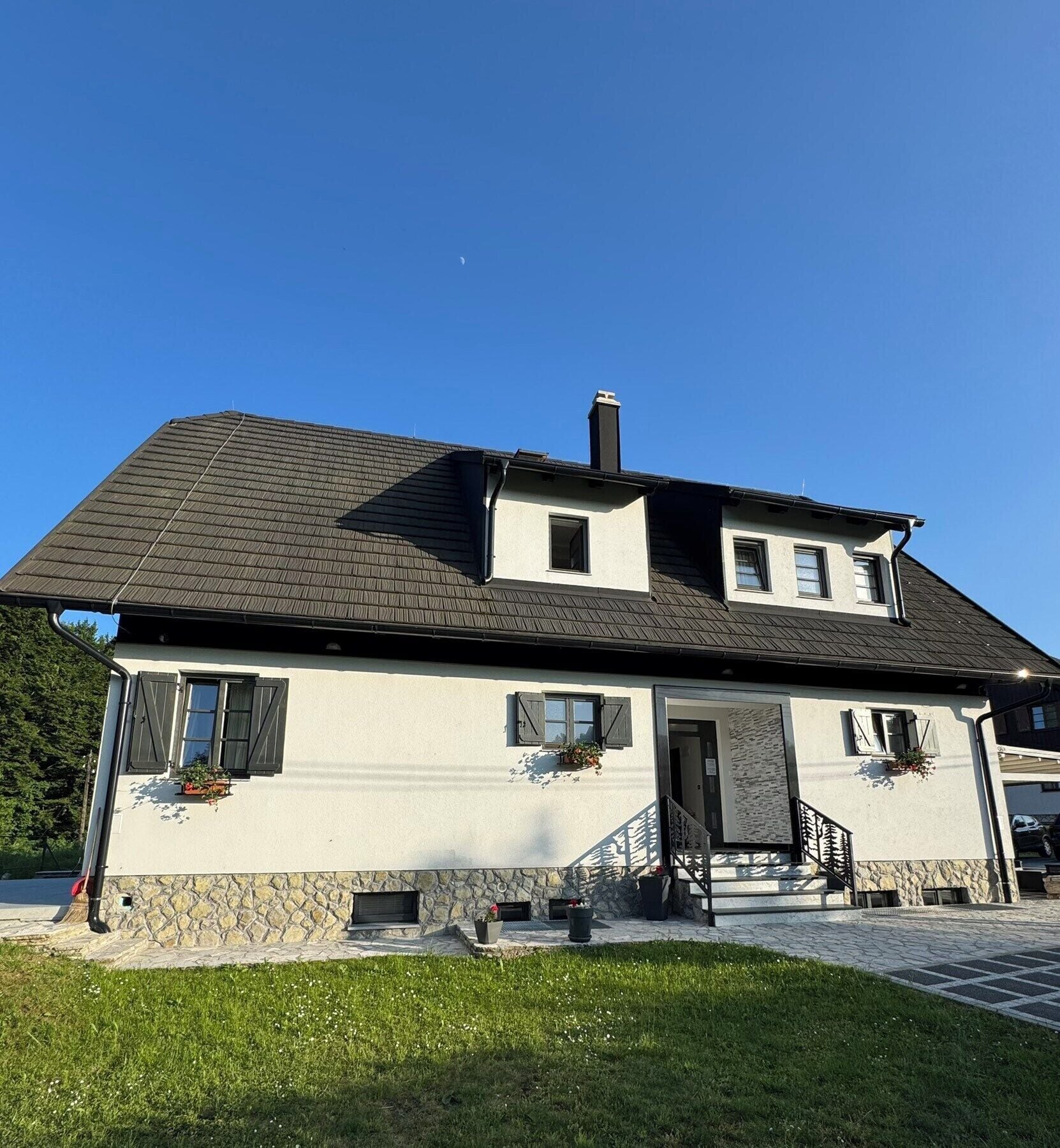 Ein zweistöckiges Haus mit Steinaußenseite, einem dunklen Dach und einer kleinen Veranda mit Stufen.